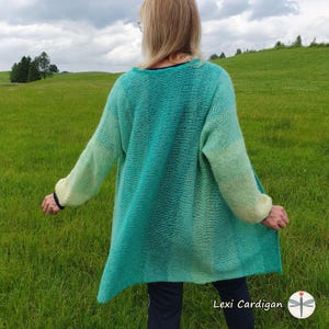 Pode incluir: Um cardigan ombré verde-azulado e verde com mangas compridas. O suéter aberto é usado por uma pessoa em pé em um campo gramado. O texto "Lexi Cardigan" é visível na parte inferior da imagem.