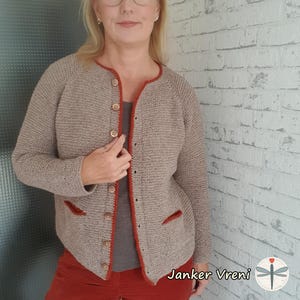 Può includere: Un cardigan beige con bordatura rossa, con chiusura a bottoni e due tasche. Il cardigan è lavorato a maglia e ha una vestibilità rilassata.