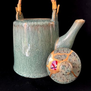 Könnte beinhalten: Eine grüne Teekanne aus Keramik mit einem Bambusgriff und einem Deckel mit goldenen Akzenten. Die Teekanne hat eine craquelée-Glasur und ein einzigartiges Design.