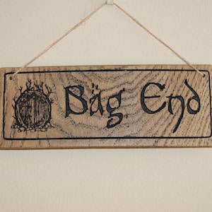 May include: A wooden sign with the words "Bag End" carved into it. The sign is hanging from a string and has a small drawing of a hobbit hole on the left side.