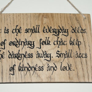 May include: Wooden sign with the quote "It is the small everyday deeds of ordinary folk that keep the darkness away. Small acts of kindness and love." The text is in black calligraphy on a light brown wood.