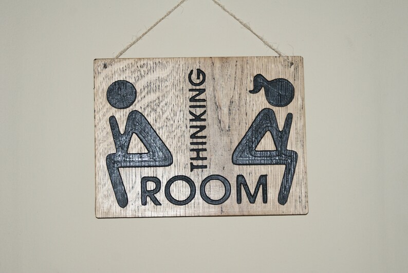 May include: A wooden sign with the text "Thinking Room" and two stick figures, one with a ponytail, sitting on a toilet.