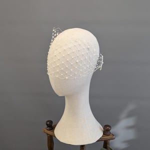 May include: A white bridal veil with pearl embellishments. The veil is made of a fine mesh fabric and is designed to be worn over the face.