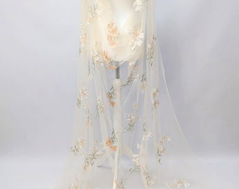 May include: White tulle fabric with embroidered floral designs in shades of peach and green.