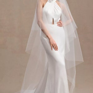 May include: A white halter-neck wedding dress with a fitted bodice and a flowing skirt. The dress is paired with a long, white veil.
