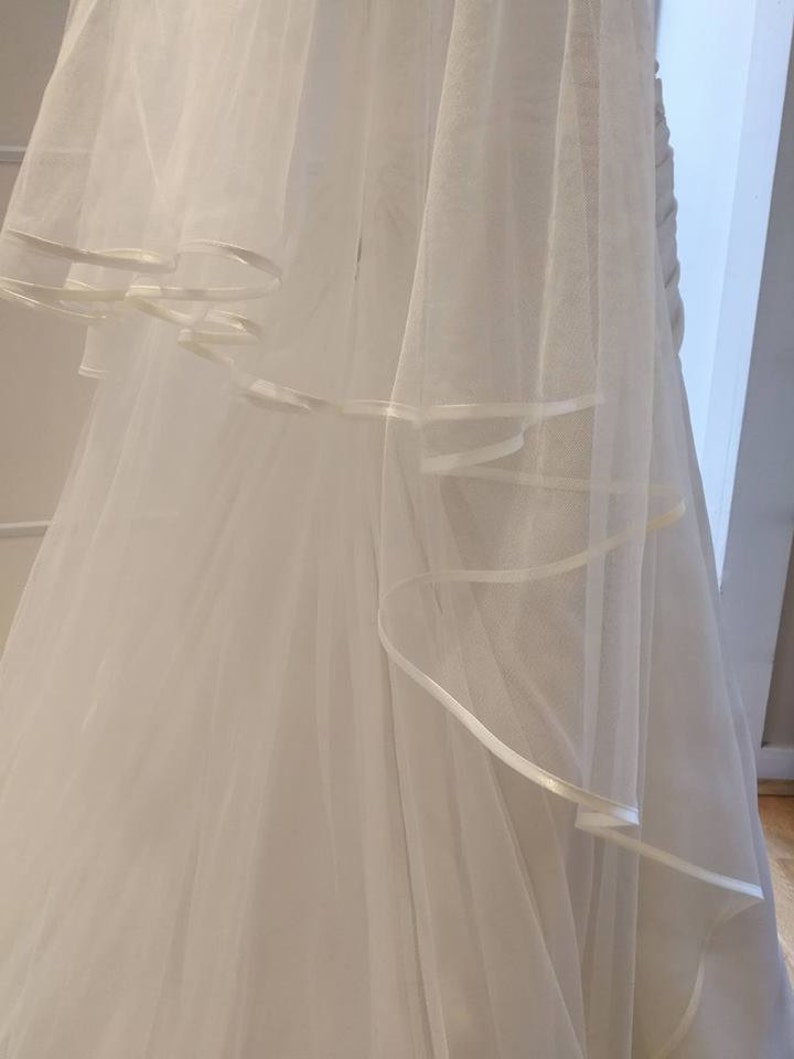 May include: A white tulle wedding veil with a satin ribbon trim. The veil is layered and has a flowing design.