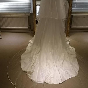 May include: A white wedding dress with a long train and a veil. The dress has a fitted bodice and a flowing skirt.