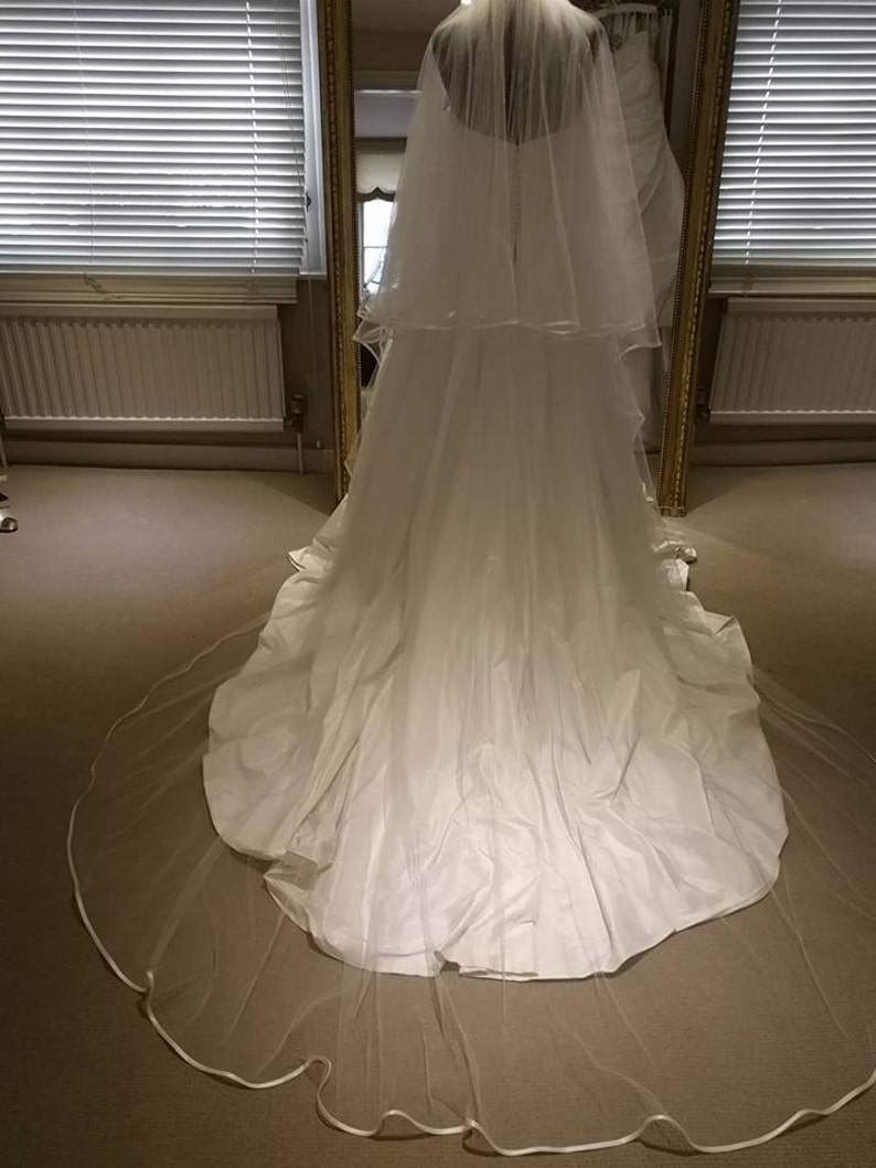 May include: A white wedding dress with a long train and a veil. The dress has a fitted bodice and a flowing skirt.