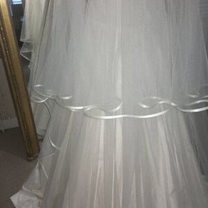 May include: A white wedding dress with a tulle skirt and a white satin ribbon trim. The dress has a long train and a fitted bodice.
