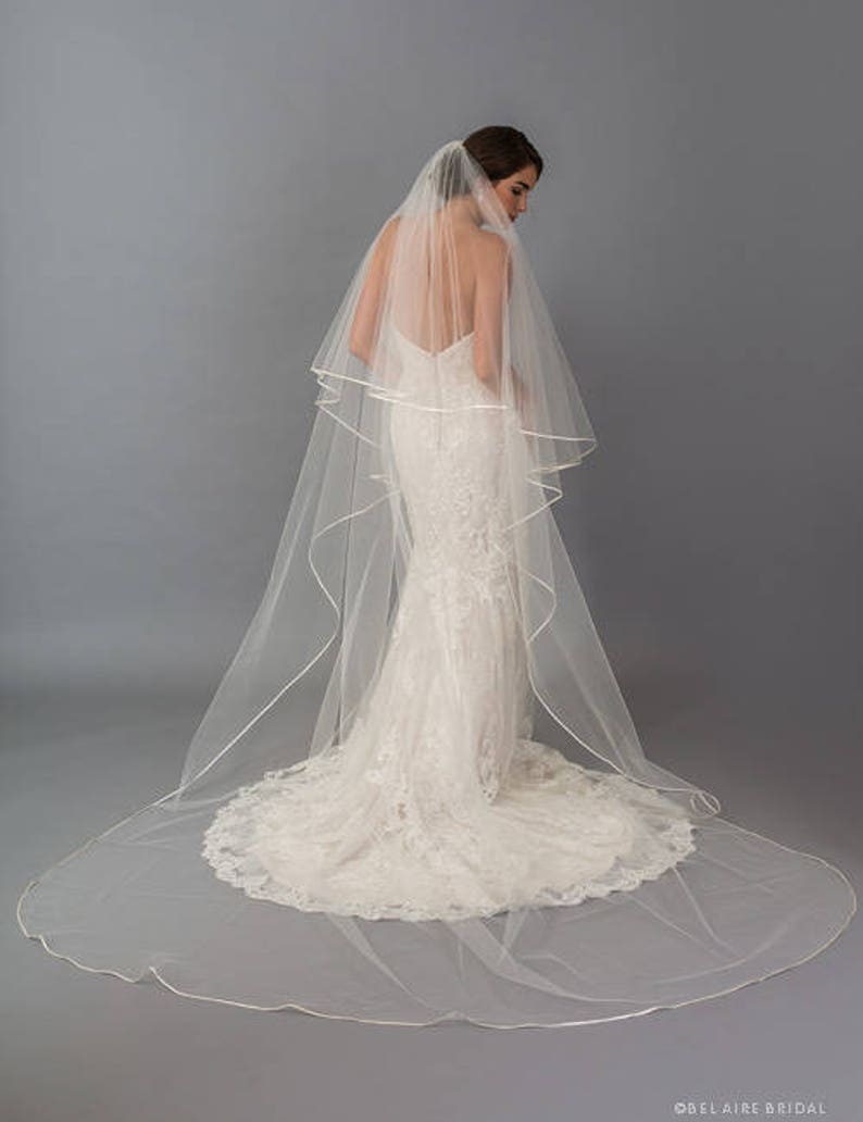 May include: A white bridal veil with a satin edge. The veil is long and flowing, with a single layer of tulle.
