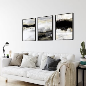 May include: Three abstract art prints in black frames. The prints feature a black, white, and gold color scheme with abstract shapes and lines.