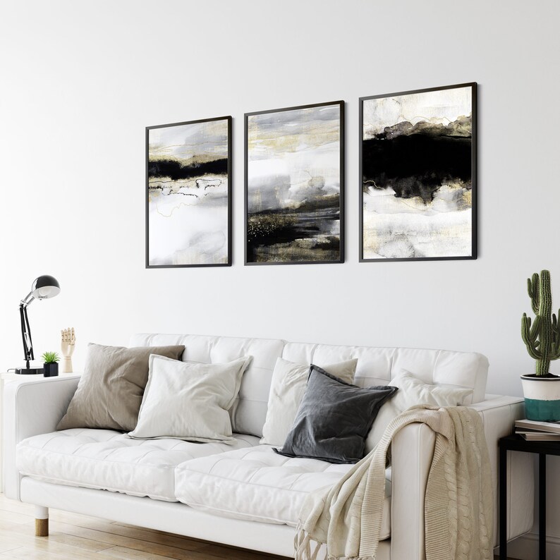 May include: Three abstract art prints in black frames. The prints feature a black, white, and gold color scheme with abstract shapes and lines.