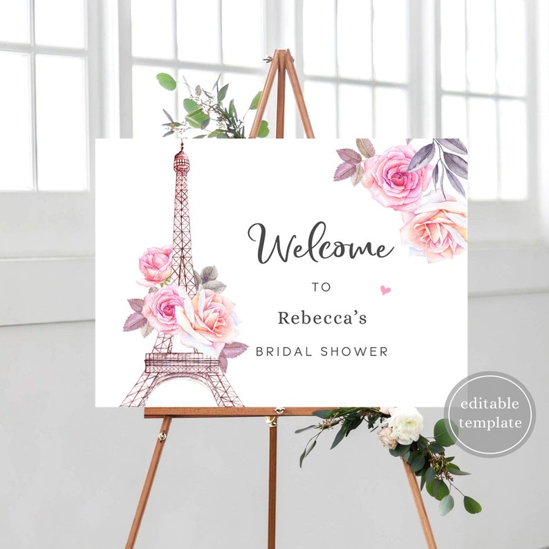 May include: A printable welcome sign for a bridal shower with a pink and white floral design and an illustration of the Eiffel Tower. The text reads "Welcome to Rebecca's Bridal Shower".