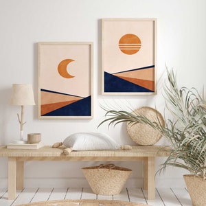 May include: Two framed prints featuring abstract geometric designs in shades of orange, brown, and blue. The prints depict a crescent moon and a sun with a pink background. The prints are hanging on a white wall above a wooden bench.