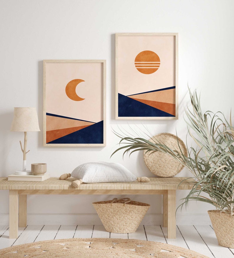 May include: Two framed prints featuring abstract geometric designs in shades of orange, brown, and blue. The prints depict a crescent moon and a sun with a pink background. The prints are hanging on a white wall above a wooden bench.