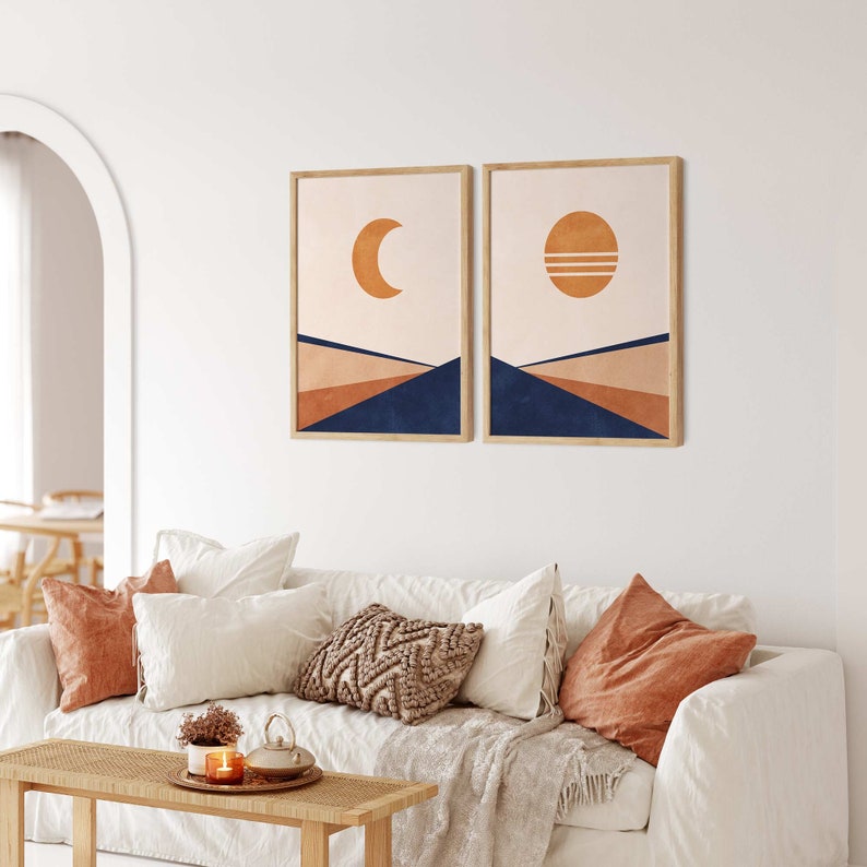 May include: Two framed prints featuring abstract geometric designs in shades of orange, brown, and blue. The prints depict a crescent moon and a sun with horizontal lines.
