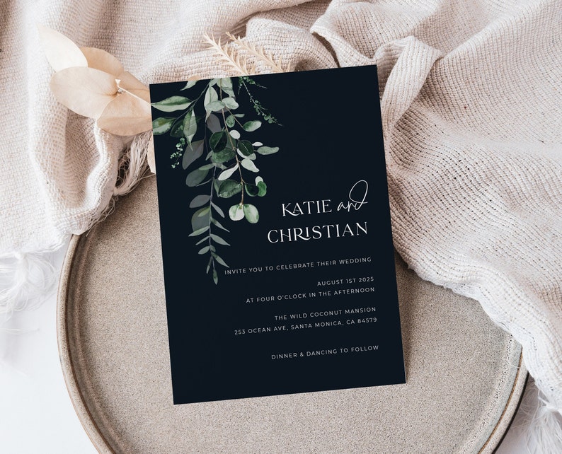 May include: A navy blue wedding invitation with elegant script and botanical accents. The invitation features the names "Katie and Christian" and event details, including the date, time, and location: The Wild Coconut Mansion in Santa Monica, CA.