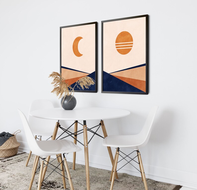 May include: Two abstract art prints with a minimalist design. The prints feature a crescent moon and a sun with a geometric pattern on a peach background. The prints are framed in black and have a navy blue geometric pattern at the bottom.