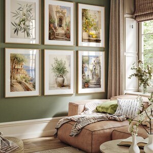 Peut inclure: Six aquarelles encadr&eacute;es repr&eacute;sentant des sc&egrave;nes italiennes, dont un citronnier, une branche d'olivier en pot et une vue d'une ville c&ocirc;ti&egrave;re. Les tableaux sont accroch&eacute;s &agrave; un mur vert dans un salon.
