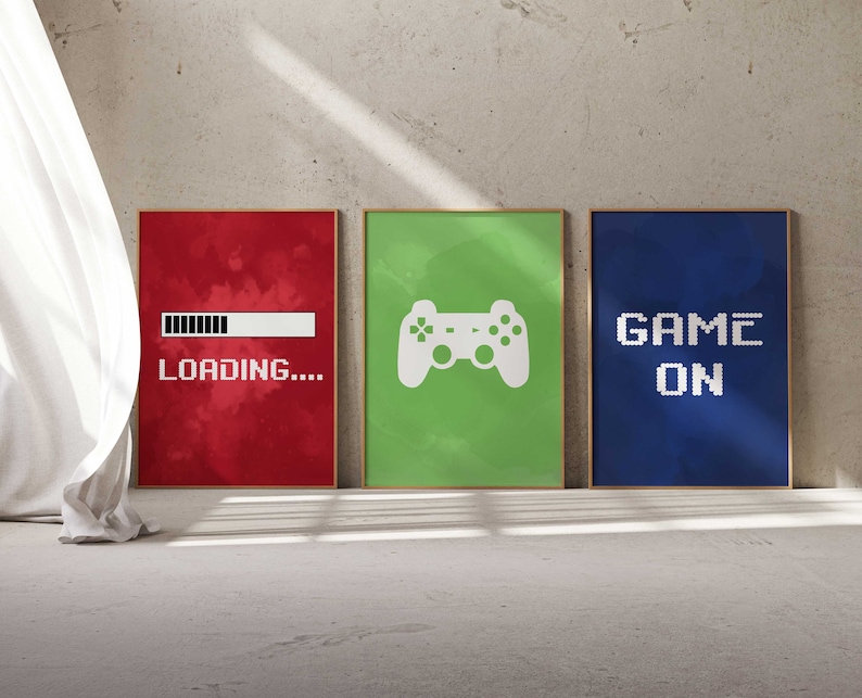 Puede incluir: Tres impresiones enmarcadas con un tema de juegos. La primera impresi&oacute;n es roja con una barra de carga blanca y el texto "CARGANDO..." La segunda impresi&oacute;n es verde con un icono de mando de videojuego blanco. La tercera impresi&oacute;n es azul con el texto "GAME ON" en blanco.