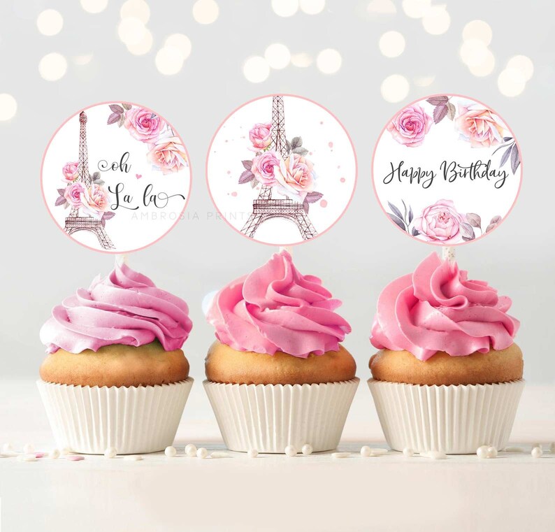 Pu&ograve; includere: Tre cupcake glassati rosa con pirottini da cupcake bianchi. Ogni cupcake &egrave; sormontato da un topper rotondo di carta con un design ad acquerello della Torre Eiffel e rose rosa. I topper dicono "Oh La La", "Buon compleanno" e un design con la Torre Eiffel e rose.