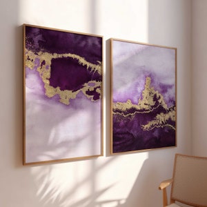Puede incluir: Dos pinturas abstractas enmarcadas con dise&ntilde;os de acuarela p&uacute;rpura y dorado. Las pinturas est&aacute;n en marcos de madera y est&aacute;n colgadas en una pared blanca.