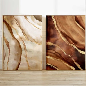 Peut inclure: Deux peintures abstraites avec des accents dor&eacute;s. La peinture de gauche a un fond brun clair avec des tourbillons blancs et dor&eacute;s. La peinture de droite a un fond brun fonc&eacute; avec des tourbillons dor&eacute;s.
