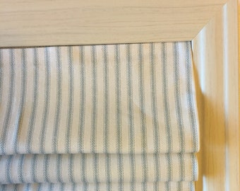 May include: A white roman shade with blue stripes. The shade is folded up and is in a wooden frame.