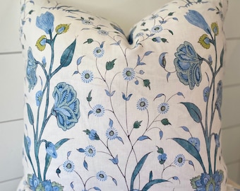 May include: A white pillow with a blue and green floral pattern. The pillow is made of a soft, linen-like fabric and features a variety of floral designs, including small blue flowers and larger blue and green flowers.