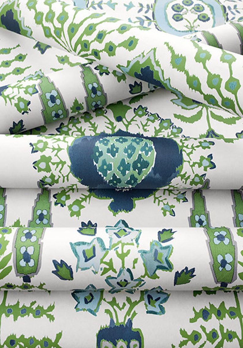 K&ouml;nnte beinhalten: Nahaufnahme eines wei&szlig;en Stoffes mit einem sich wiederholenden Muster aus gr&uuml;nen und blauen floralen Designs. Der Stoff ist in mehreren Schichten gefaltet, wodurch die komplizierten Details des Musters hervorgehoben werden.
