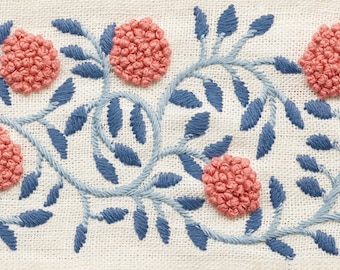 May include: A close-up of a white fabric with blue embroidered vines and pink embroidered flowers. The flowers are made with a technique called French knots.