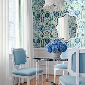 K&ouml;nnte beinhalten: Ein Esszimmer mit einem Glastisch und vier wei&szlig;en St&uuml;hlen mit hellblauen Kissen. Die St&uuml;hle sind um den Tisch herum angeordnet. Die W&auml;nde sind mit einer gr&uuml;n-blauen Blumentapete bedeckt. Eine wei&szlig;e H&auml;ngeleuchte aus Weidengeflecht h&auml;ngt von der Decke. Ein Spiegel mit einem gewellten Rand h&auml;ngt an der Wand. Ein Strau&szlig; blauer Hortensien steht auf dem Tisch.