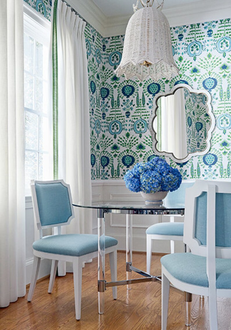 K&ouml;nnte beinhalten: Ein Esszimmer mit einem Glastisch und vier wei&szlig;en St&uuml;hlen mit hellblauen Kissen. Die St&uuml;hle sind um den Tisch herum angeordnet. Die W&auml;nde sind mit einer gr&uuml;n-blauen Blumentapete bedeckt. Eine wei&szlig;e H&auml;ngeleuchte aus Weidengeflecht h&auml;ngt von der Decke. Ein Spiegel mit einem gewellten Rand h&auml;ngt an der Wand. Ein Strau&szlig; blauer Hortensien steht auf dem Tisch.