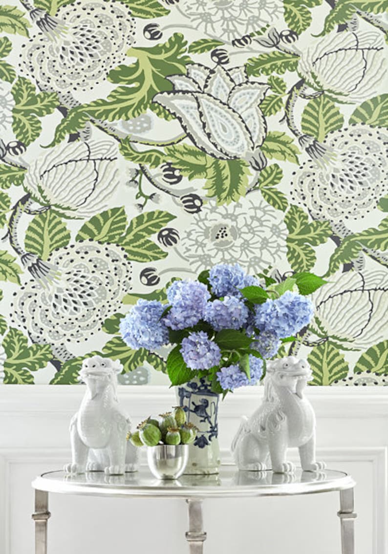 Pu&ograve; includere: Due statuette di foo dog in ceramica bianca su un tavolo argentato con un bouquet di ortensie blu in un vaso di porcellana blu e bianco. Lo sfondo &egrave; una carta da parati bianca con un motivo floreale verde e grigio.