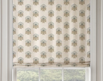 May include: A white roman shade with a repeating pattern of blue and brown stylized flowers. The shade is pulled up to reveal a window with a view of a green lawn and trees.