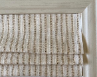 May include: Close-up of a beige and white striped fabric, possibly a window treatment or curtain. The fabric is folded in layers, with a light wooden frame surrounding it. The stripes are vertical and evenly spaced.