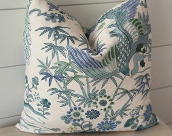 May include: Square decorative pillow with a cream background and a blue and green floral and bird pattern. The design includes bamboo stalks, flowers, and a stylized bird. The pillow is placed on a neutral-colored surface.