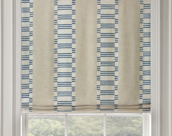 May include: A white roman shade with blue geometric stripes. The shade is pulled up to reveal a window with a view of a green lawn and trees.