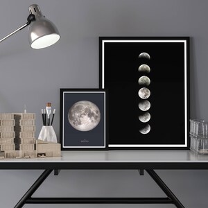May include: A black and white photo of the moon in different phases, framed and displayed on a desk with a lamp, a model building, and a clear storage bin.