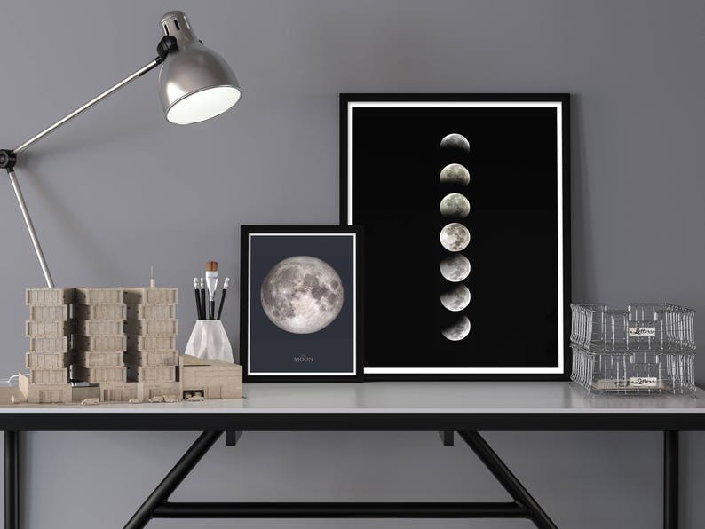 May include: A black and white photo of the moon in different phases, framed and displayed on a desk with a lamp, a model building, and a clear storage bin.