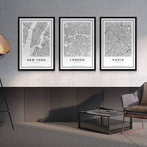 May include: Three framed city map prints. The prints feature black and white detailed maps of New York, London, and Paris. Each print has the city name at the bottom. The frames are black, and the prints are displayed on a wall.