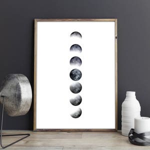 Op de afbeelding: Een zwart-witte print van de maan in verschillende fasen, ingelijst in een eenvoudig houten frame.