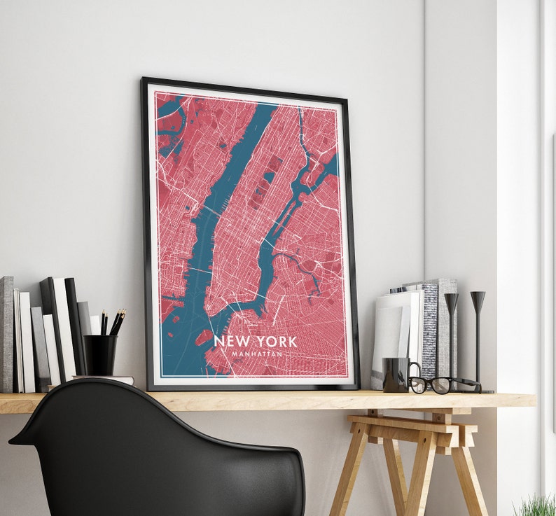 May include: Framed New York City map print in a modern style. The map features a red and blue color scheme, with the city's streets and waterways clearly defined. The text "NEW YORK MANHATTAN" is displayed at the bottom of the map. The print is displayed on a wooden desk.
