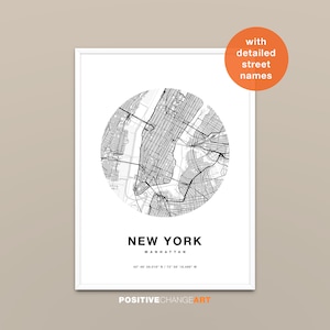 May include: A framed black and white map print of Manhattan, New York. The map is circular and includes detailed street names. The words "NEW YORK" are printed below the map, along with the coordinates. The print is in a white frame.