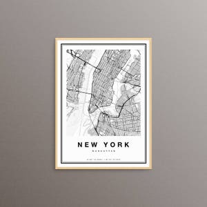 May include: A framed black and white map of Manhattan, New York. The map is detailed with streets and waterways. The text "NEW YORK MANHATTAN" is centered at the bottom, with coordinates below. The frame is a light wood color.