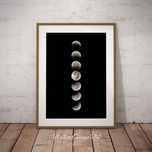 May include: A black and white photo of the moon in various phases, displayed in a vertical line against a black background. The image is framed in a simple, light brown frame.