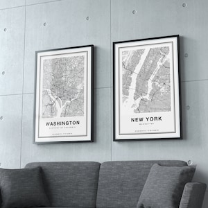 May include: Two framed black and white city map prints. One map is of Washington, District of Columbia, and the other is of New York, Manhattan. The prints are displayed above a gray sofa against a concrete wall.
