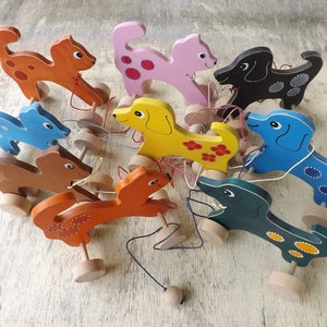 Può includere: Un set di nove giocattoli di legno a traino a forma di animali. I giocattoli sono dipinti con colori vivaci e hanno dettagli come macchie e fiori. Ogni giocattolo ha una corda attaccata e una ruota di legno sul fondo.