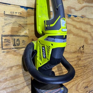 May include: A green and black Ryobi hedge trimmer with a curved handle and blade guard. The trimmer has a black handle and a yellow body. The blade is red and silver. The trimmer is hanging on a wooden surface.