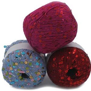 May include: Three colorful yarn skeins. One is a deep magenta, another is a light blue with colorful sequins, and the third is a deep red with red sequins. The yarn is tightly wound and ready for crafting projects.